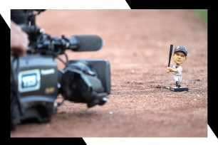 A Babe Ruth bobblehead sits on the ground next to a camera for scale.