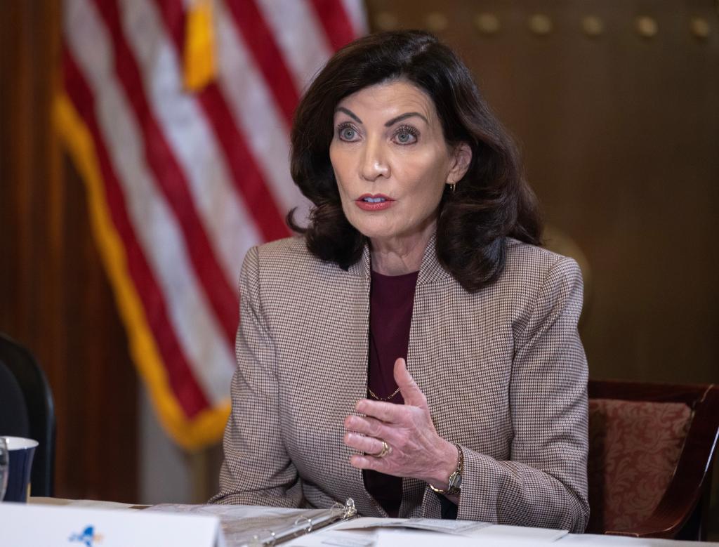 Gov. Kathy Hochul in a blazer sitting in front of an american flag