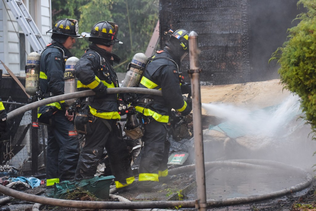 Firefighters hold a hose as they put water on the fire. 