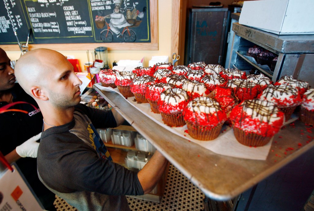A worker holding a cooking tray of freshly baked cupcakes.