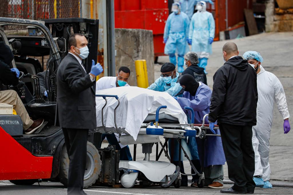A body wrapped in plastic that was unloaded from a refrigerated truck is handled by medical workers wearing personal protective equipment due to COVID-19 concerns