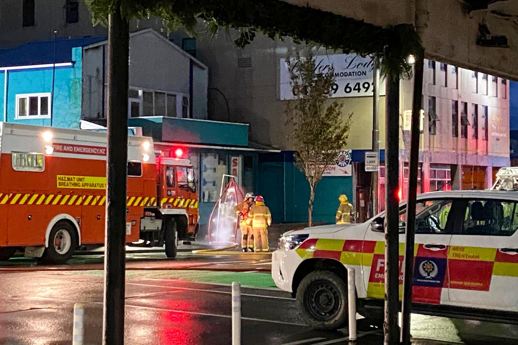 Firefighters stand outside a fire at a hostel