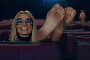 Margot Robbie as Sharon Tate sitting in movie theater with dirty feet propped up on seat in front of her