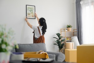 A young woman hangs a picture up.