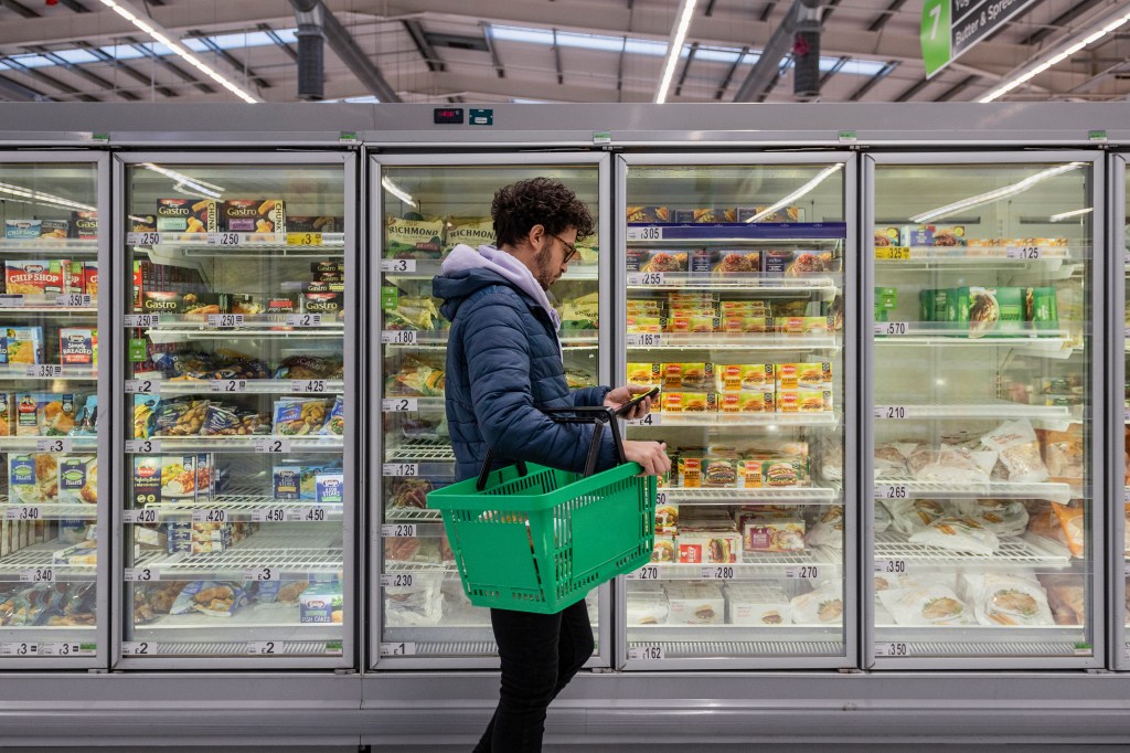 Man with shopping basket walking past frozen section.