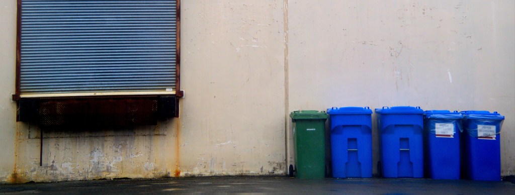 Recycling bins in a line against a wall.