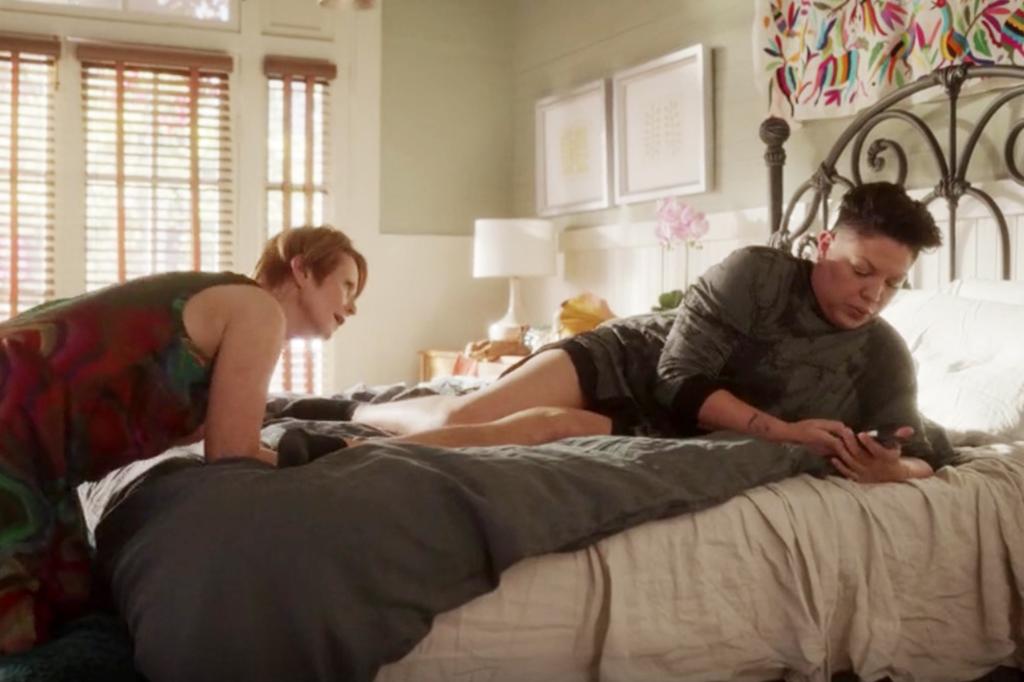 Miranda (Cynthia Nixon) bends over a bed while Che (Sara Ramirez) lounges on it. 
