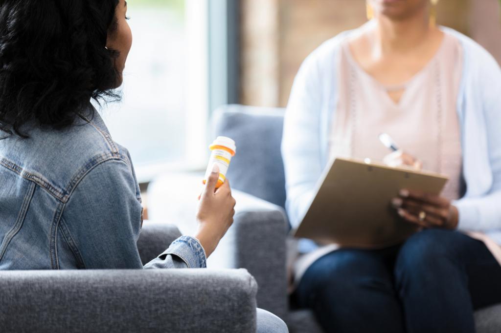 The young woman holds onto the prescription bottle while she listens to  medical professional