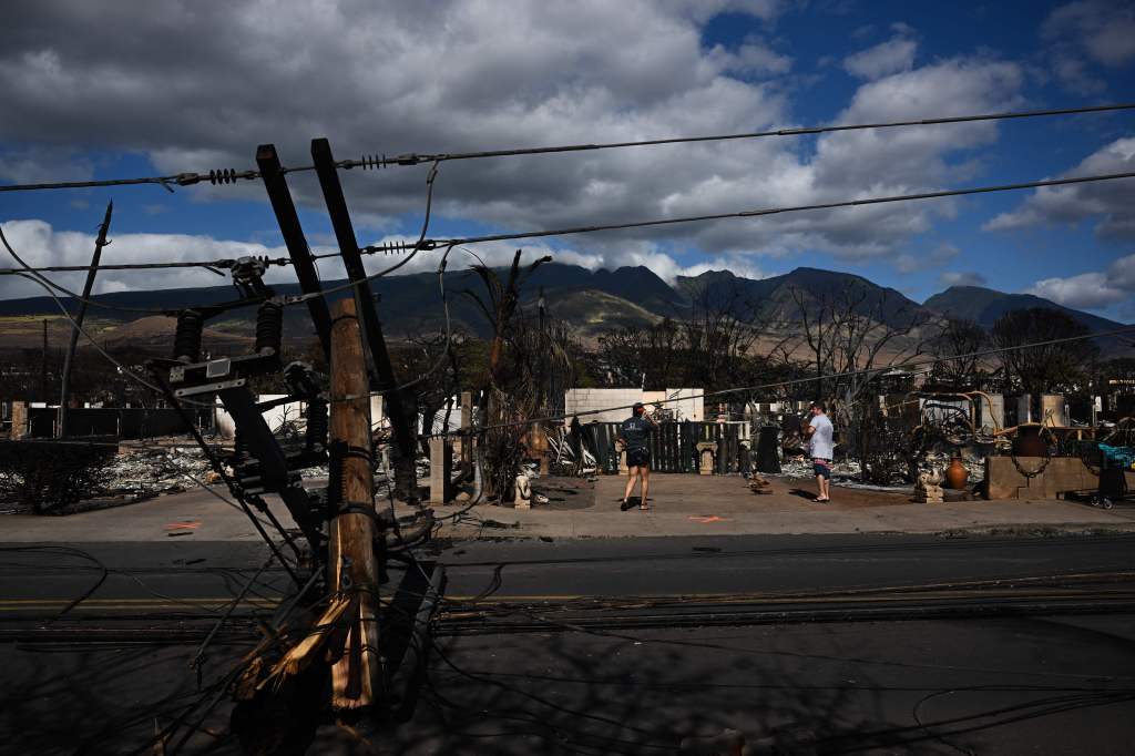 Downed power lines block a road as people feed chickens outside a burnt home in the aftermath of a wildfire in Lahaina.