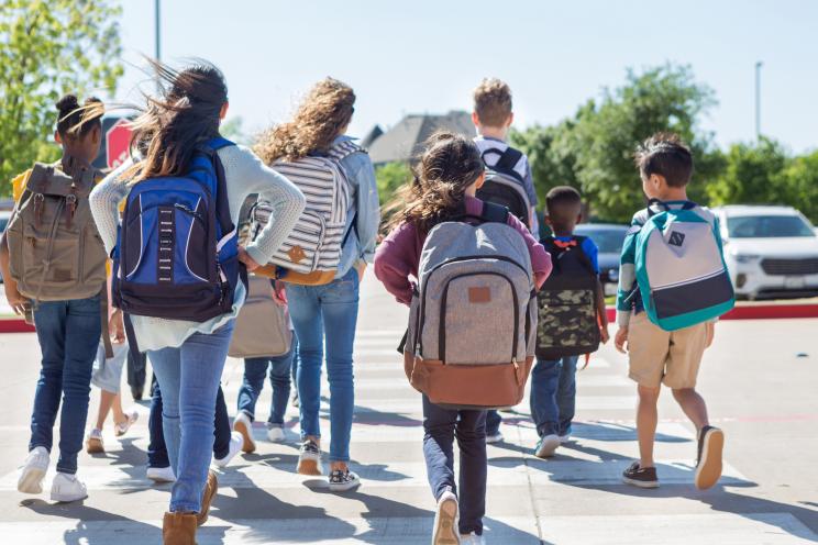 A diverse group of students walk safely on crosswalk to the parking lot.