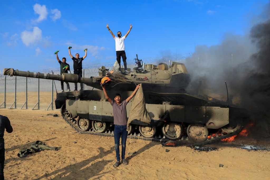 Palestinians celebrate as an Israeli military vehicle burns after it was hit by Palestinian gunmen who infiltrated areas of southern Israel, at the Israeli side of Israel-Gaza border, October 7, 2023.