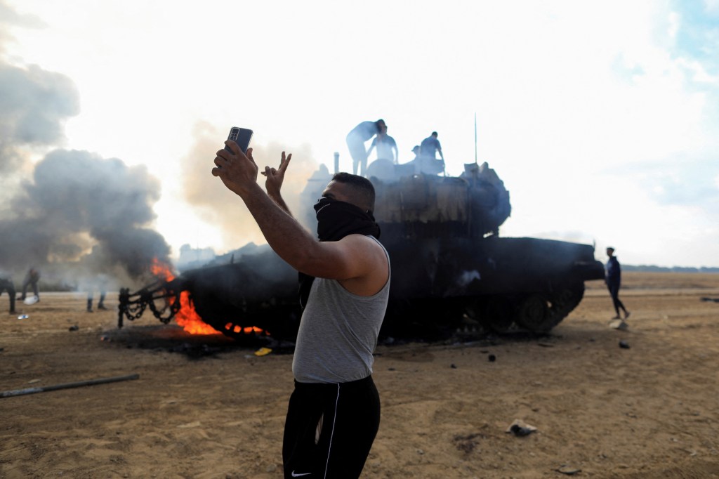 A Palestinian man takes a selfie in front of a burning Israeli military vehicle after it was hit by Palestinian gunmen who infiltrated areas of southern Israel on Oct. 7, 2023.