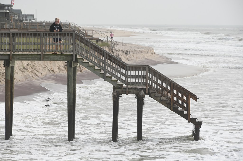 A man looks at eroded beech from washed-away wooden stairway