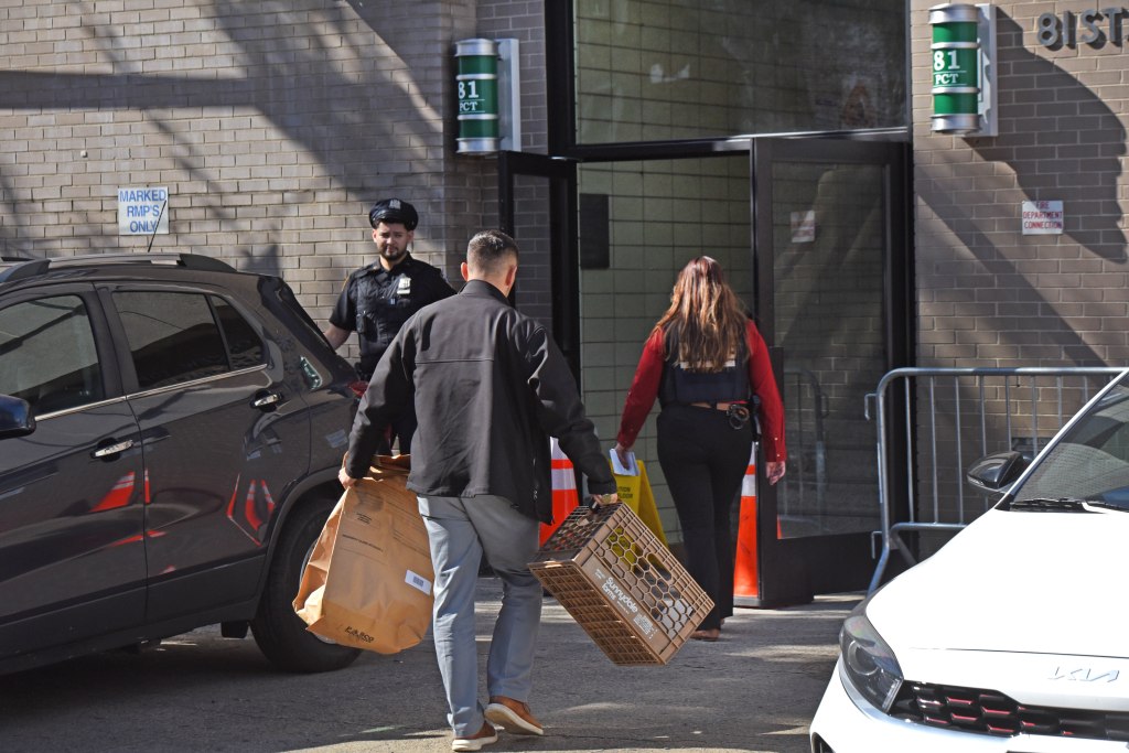 Detectives bring evidence in a brown bag and box into the 81st Precinct. 