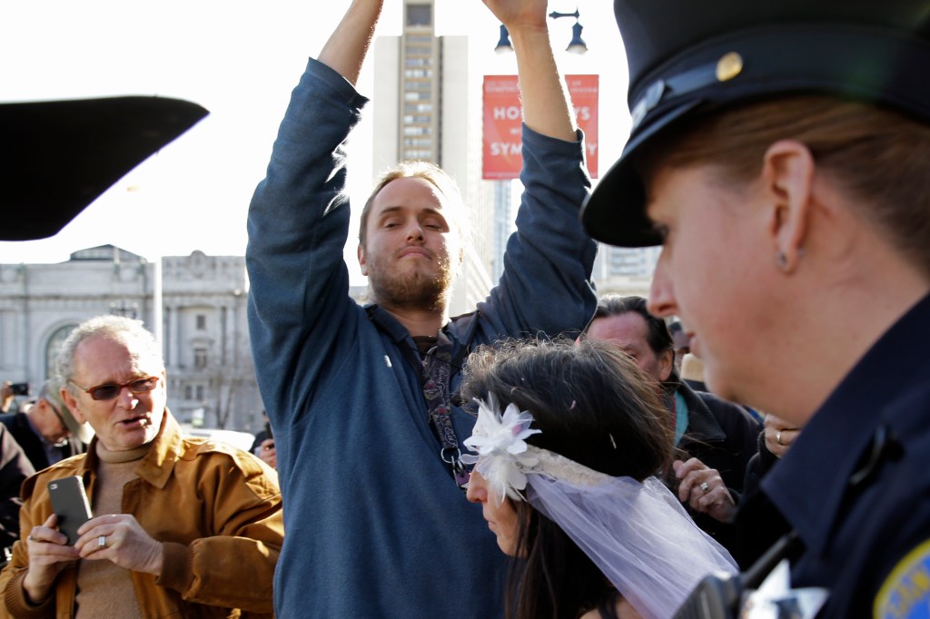 David DePape, center, records Gypsy Taub being led away by police after her nude wedding outside City Hall on Dec. 19, 2013, in San Francisco. DePape is accused of breaking into House Speaker Nancy Pelosi's California home and severely beating her husband with a hammer. DePape was known in Berkeley, Calif., as a pro-nudity activist who had picketed naked at protests against local ordinances requiring people to be clothed in public.