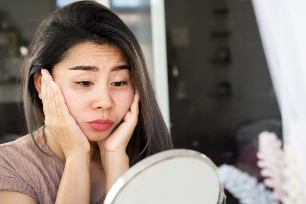 Woman gazing into small mirror, sad