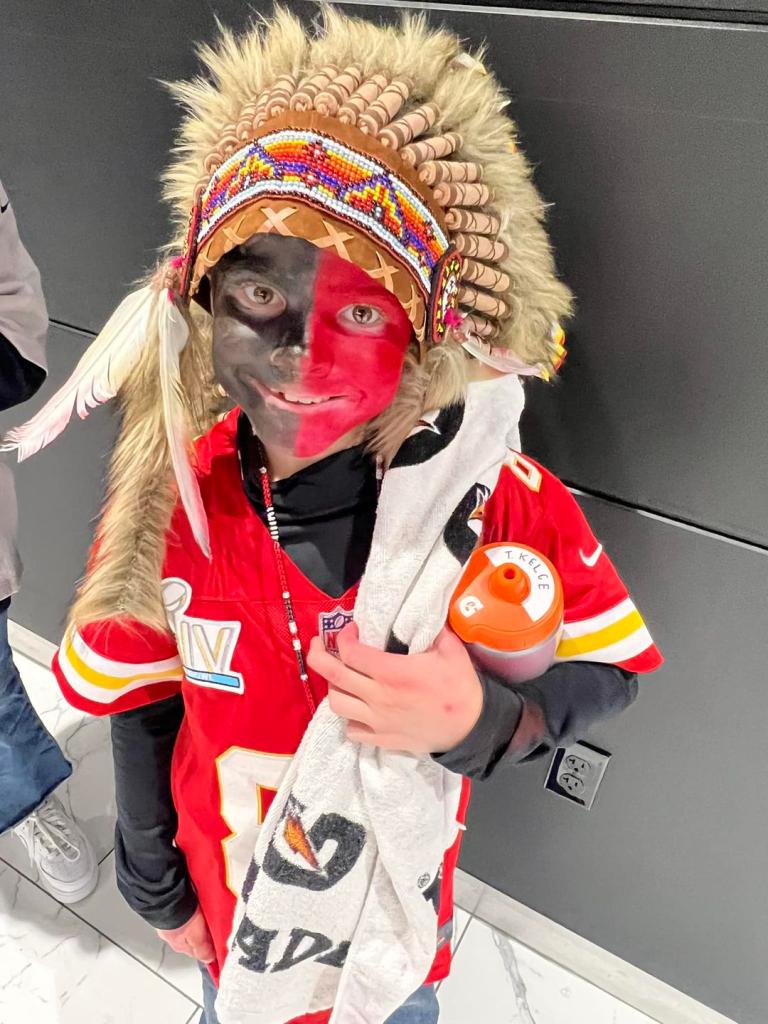 Holden Armenta with his face painted red and black and wearing a Native headdress.  