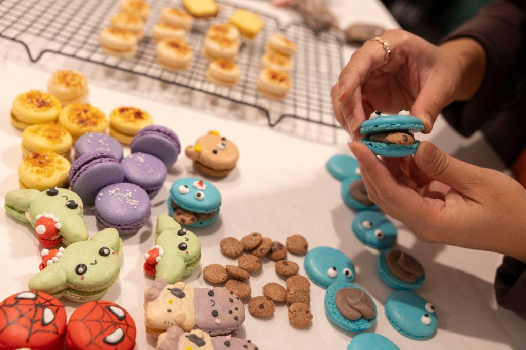 stephanie tran holding  cookie monster cookie, with different character cookies on table including spider-man, grogu and hello kitty