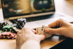 Hand of playing cards and gambling chips next to a computer.