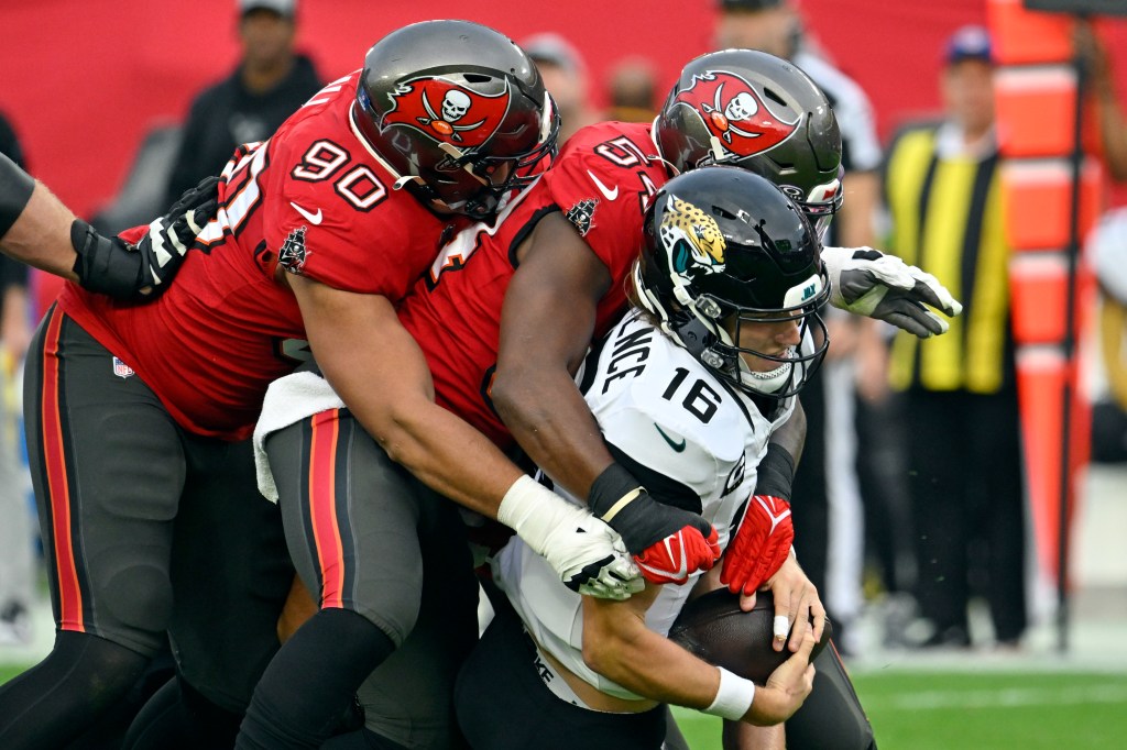 Tampa Bay Buccaneers defensive end Logan Hall (90) and linebacker Lavonte David, center, sack Jacksonville Jaguars quarterback Trevor Lawrence (16) during the first half of an NFL football game Sunday, Dec. 24, 2023, in Tampa, Fla.