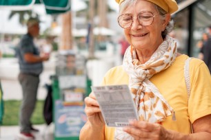 An older woman holds a scratch-off lottery ticket.