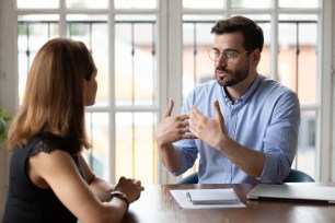 Confident male boss leader in eyeglasses explaining project details to new female employee at meeting. Concentrated young woman job applicant listening to hr manager questions at interview in office.