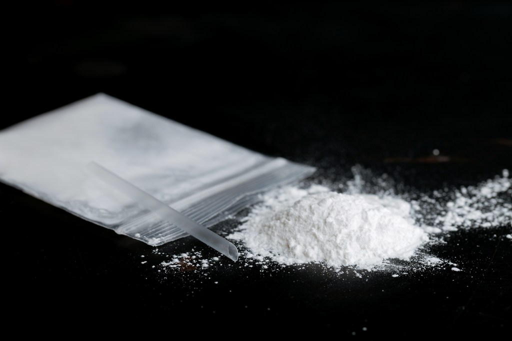 ketamine drugs and plastic straw on bag of white powder
on black wood background.Drug epidemic concept.