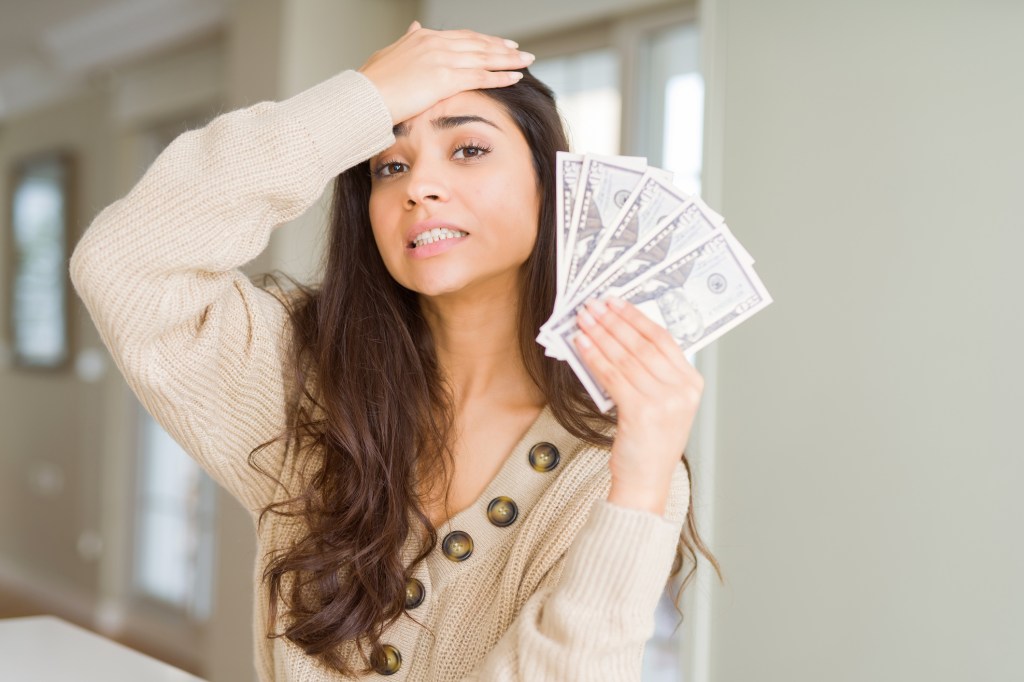 Young woman holding 50 dollars bank notes stressed with hand on head.
