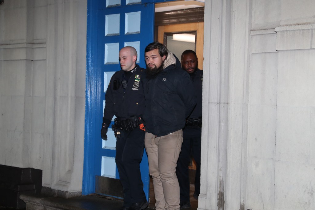 David Crowe being walked out of the 1st Precinct by a group of men at night.