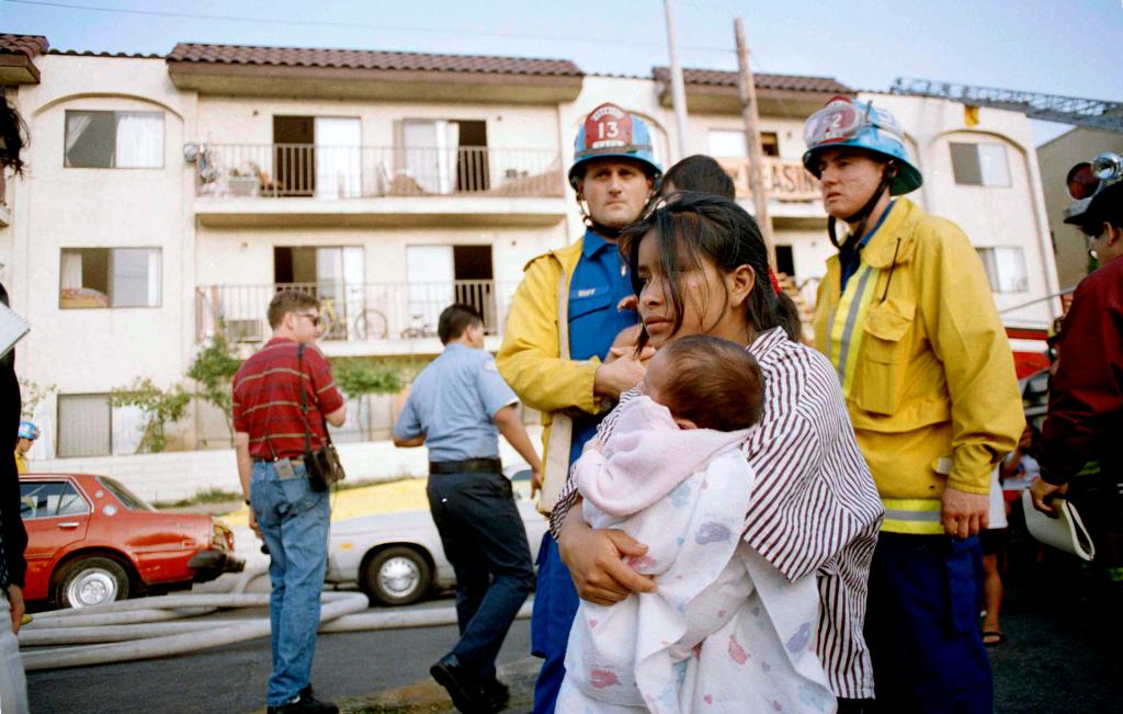 In this May 3, 1993, file photo, May Isabela Diego holds her infant son Pedro in the aftermath of a fire in an apartment complex in the Westlake section of Los Angeles