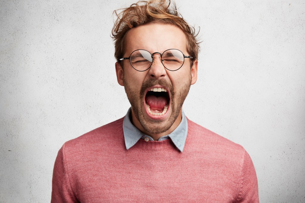 Emotional mad crazy young male screams loudly and with anger, being stressed and in panic, frowns face, isolated over white concrete wall. Negative human emotions, feelings, reaction concept