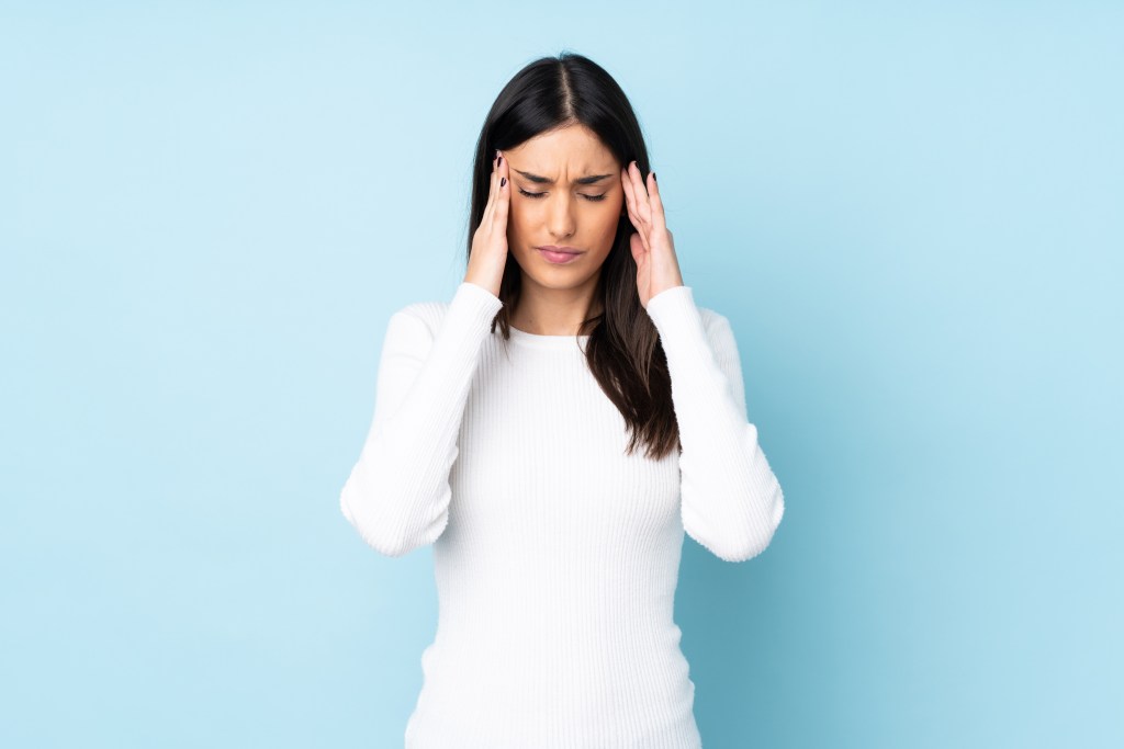 Young caucasian woman isolated on blue background with headache