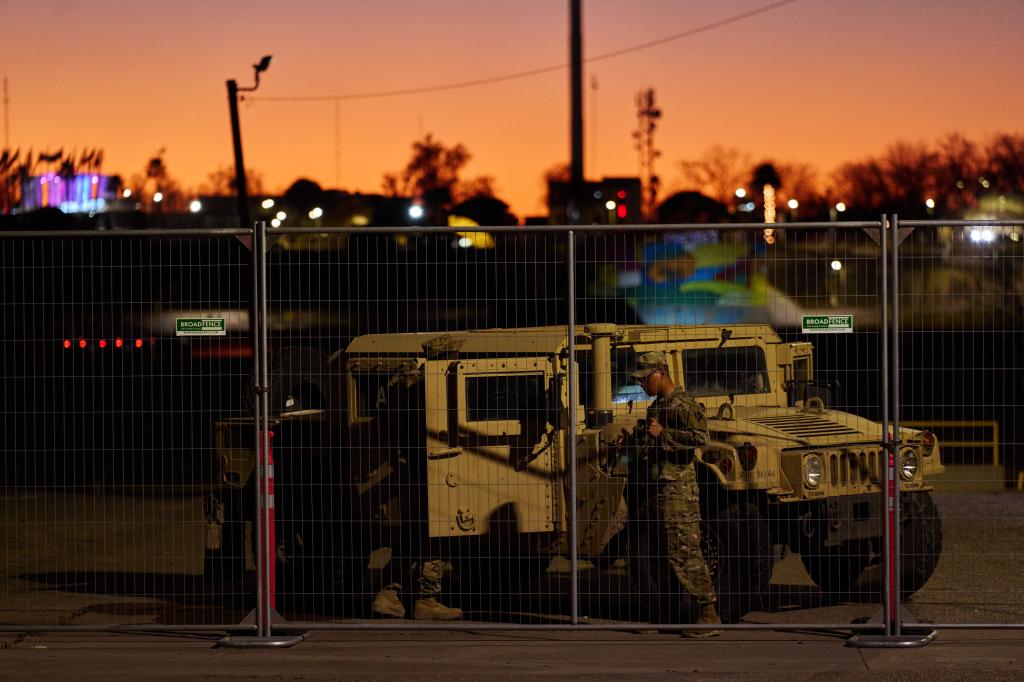 Soldier standing next to military vehicle in Shelby Park, Eagle Pass, Texas, with concertina wire fence in the background.