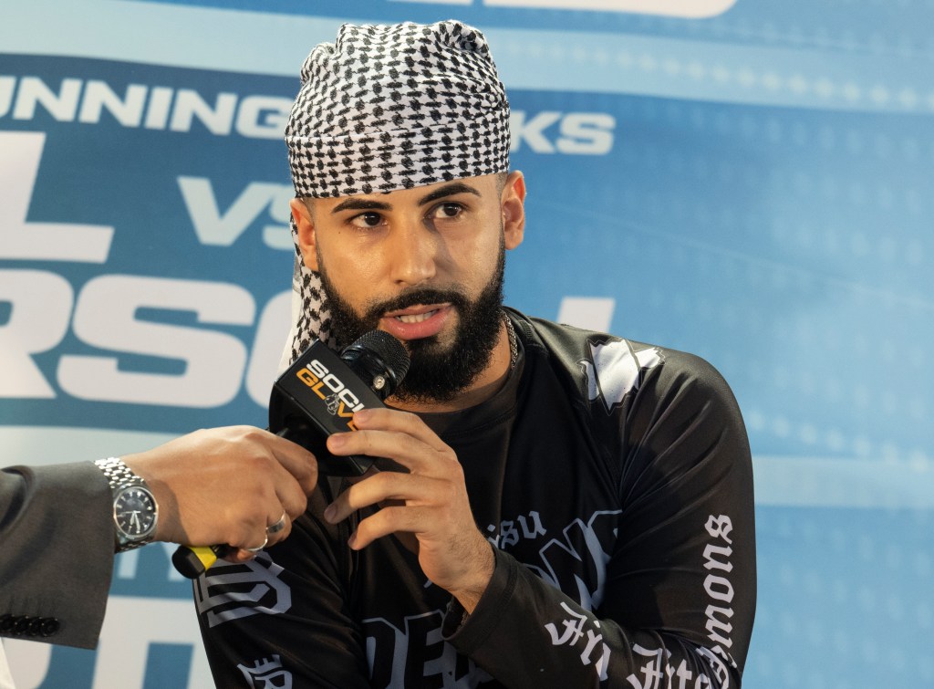 Adam Saleh speaking at news conference with kefiyah on head.