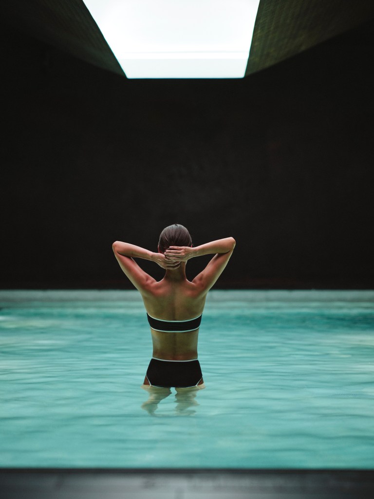 A woman in a black bikini, seen from behind, stands in a pool at Bathhouse in Flatiron. 