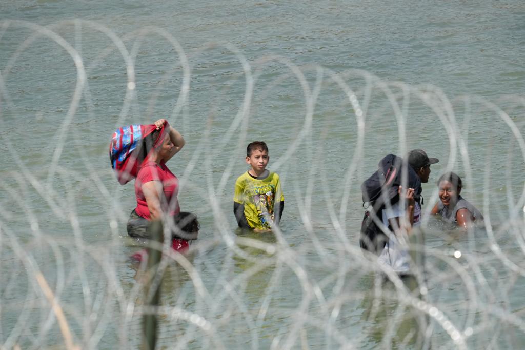A group of migrants standing in the Rio Grande River, searching for an opening in a razor wire barrier to enter Texas.