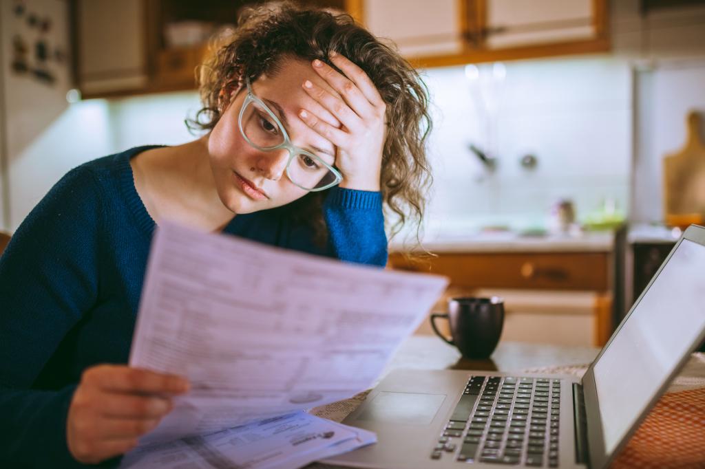 Young brunette curly female reading her bill papers, looking stressed.