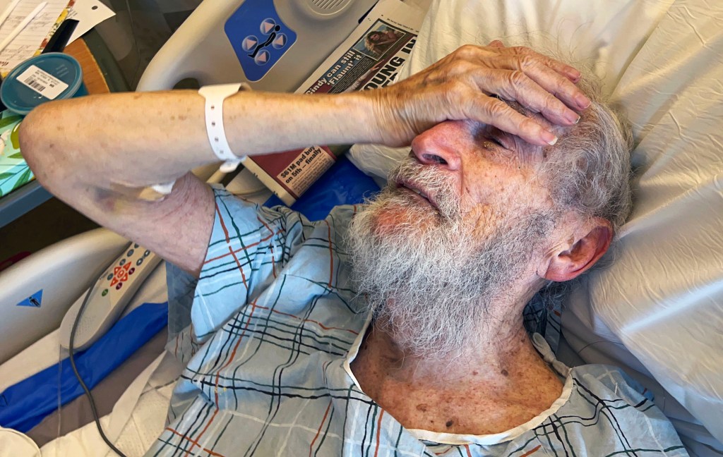 a man lying in a hospital bed with his hand on his forehead