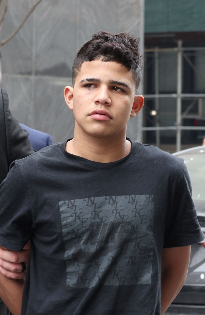 A person in a black shirt they're being escorted by police officers on a street in Manhattan, NY.