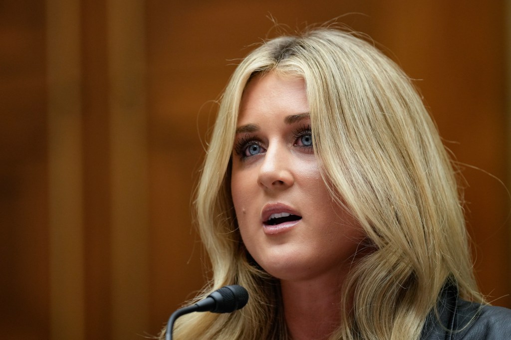 A blonde woman speaking into a microphone during a congressional hearing on Title IX and gender identity with Capitol Hill in background.