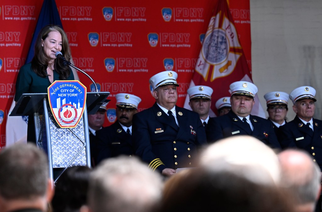 FDNY Commissioner Laura Kavanaugh speaks at a podium with the fdny symbol on it as chiefs in formal dress uniform stand nearby