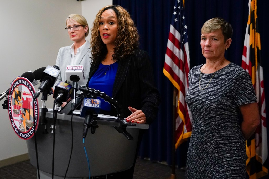 Maryland State Attorney Marilyn Mosby stands with two women at a news conference, speaking into microphones.