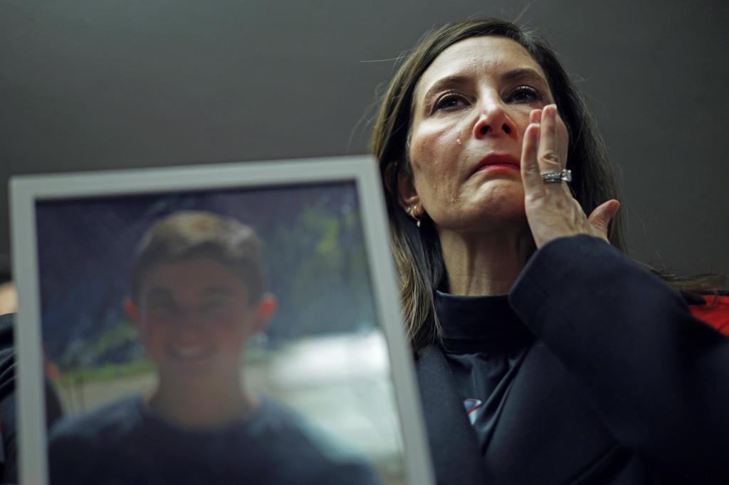 A mother wipes a tear from her face as she holds a photograph of her deceased son Nate.