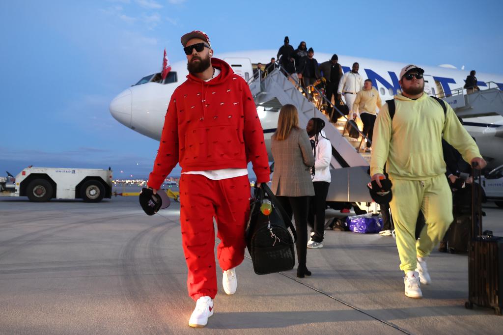 Travis Kelce in red suit walking down a plane - Super Bowl LVIII Team Arrivals.