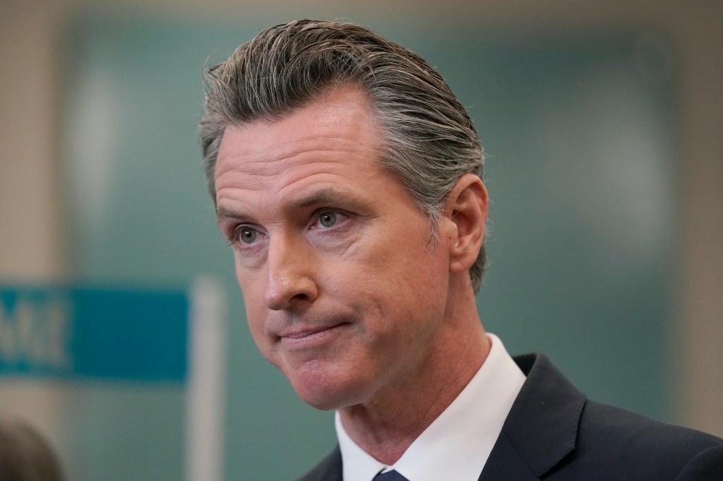 Governor Gavin Newsom speaking at a news conference, with a blurred background of an audience.