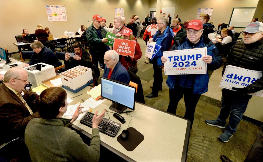 People standing with posters in a room submitting nomination papers to the State Board of Elections for Republican presidential candidate Donald Trump.