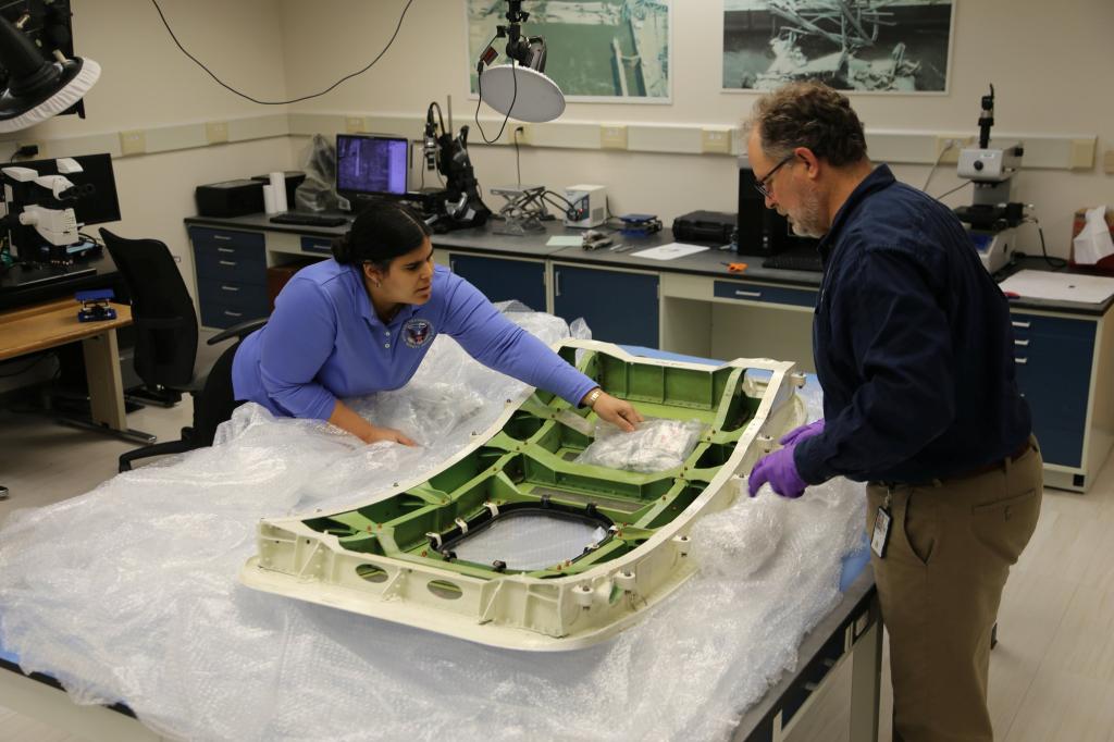 Two people unpacking a plastic door plug in a laboratory setting.