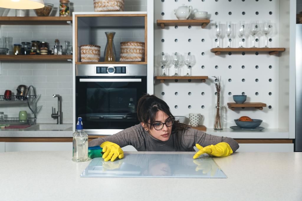 a woman wearing gloves and cleaning a kitchen counter.