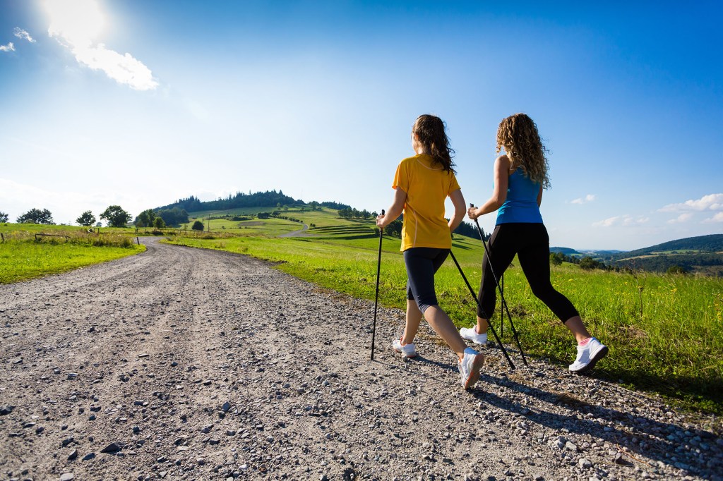 Nordic walking - two women walking on a gravel road outdoor.