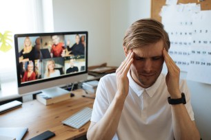 A man holding his head in front of a computer screen due to fatigue from digital meetings during remote work.